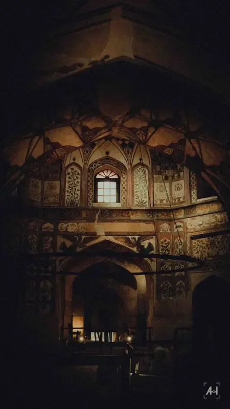 Painted frescoes and a lit window inside a Mughal-era hall at night