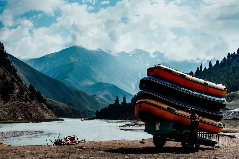 Stacked rafts from the Fairy Meadows Adventure Club beside a glacial river under the mountains