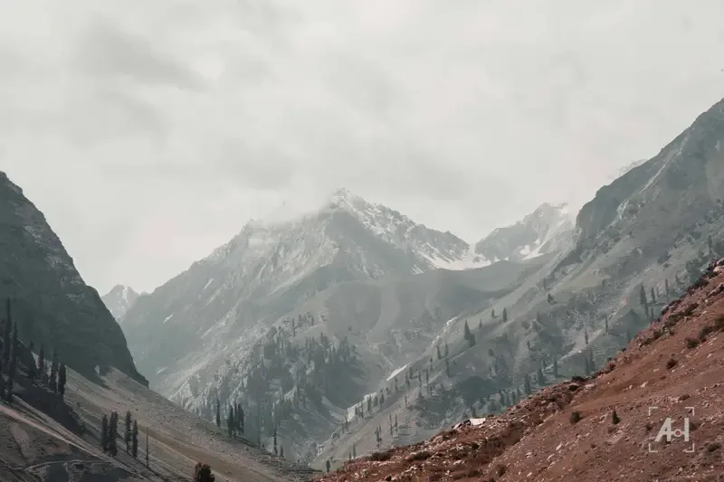 Mist over a snowy peak above a red-earth valley