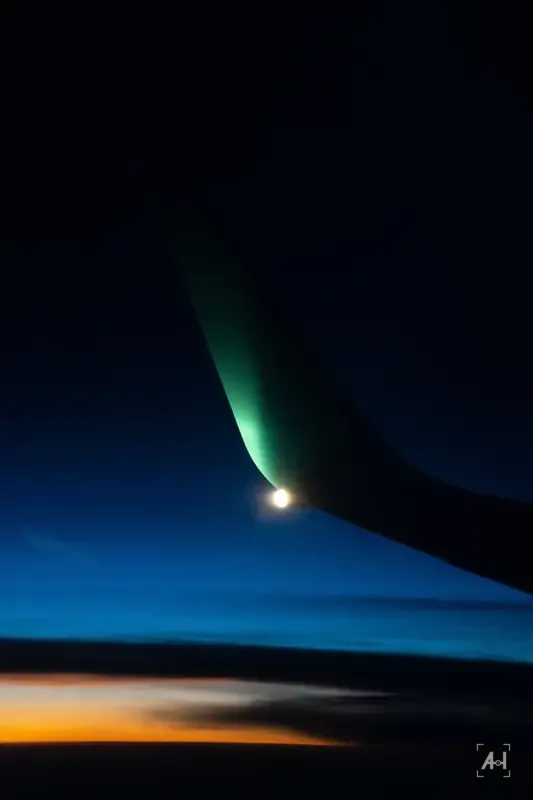 An aircraft wingtip glowing green against a deep blue dawn sky