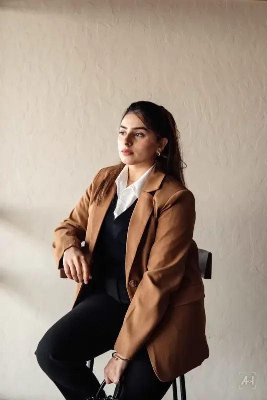 A model in a camel coat on a studio stool, for Hiba