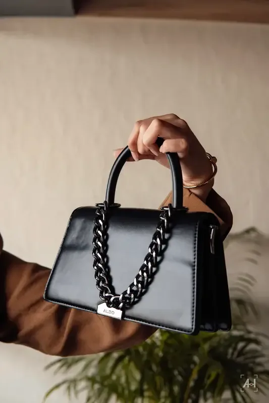 A black handbag held up against a warm plaster wall