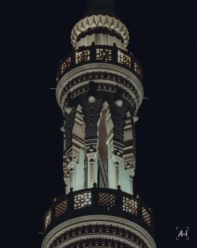 The carved balconies of a minaret lit against the night
