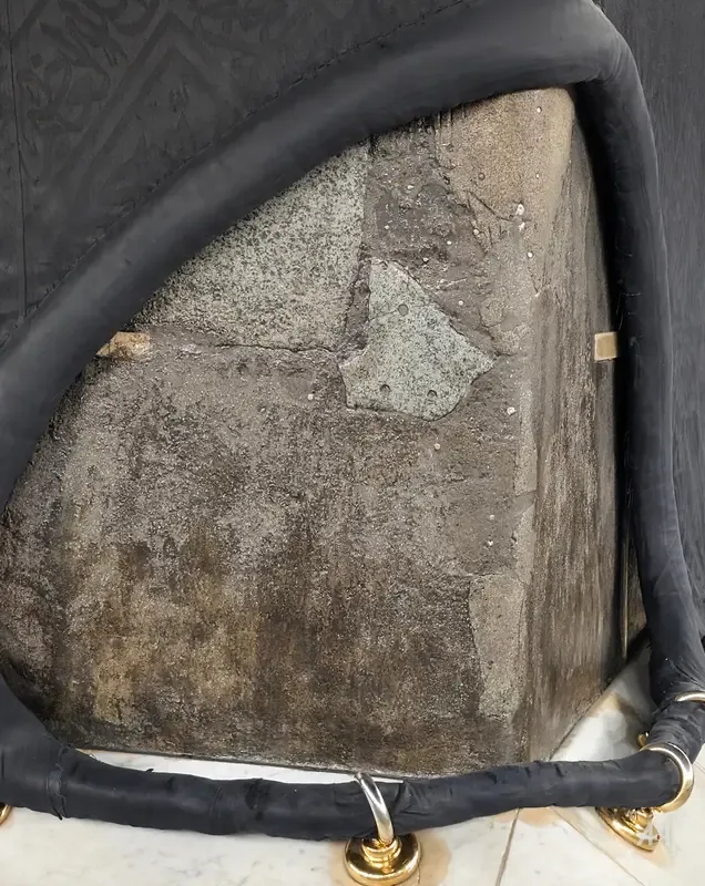 The worn stone at the corner of the Kaaba framed by the kiswa's edge