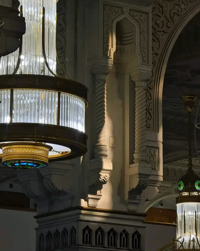 A crystal chandelier beside a carved stone column inside the Grand Mosque