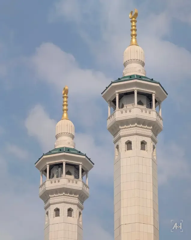 Two white minarets of the Grand Mosque with gold finials against soft clouds