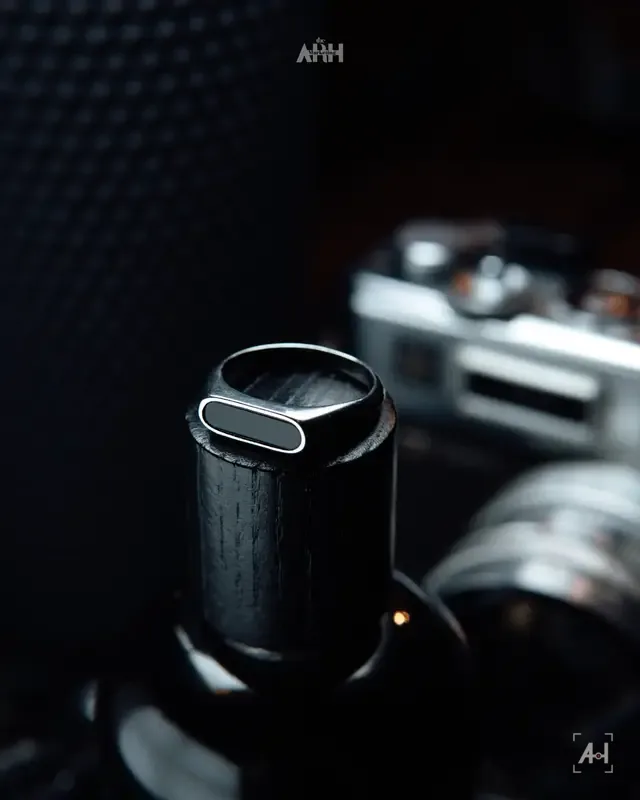 An onyx signet ring on a wooden bottle cap, a rangefinder blurred behind