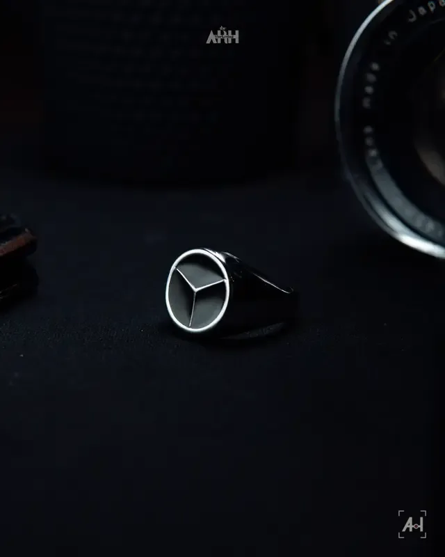 The Mercedes-star signet ring on black cloth beside an old lens