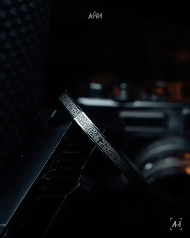 A steel bangle engraved with a prayer, leaning on black equipment in shadow
