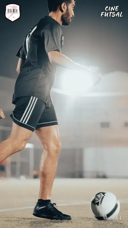A player in Adidas shorts on the ball, backlit by a floodlight
