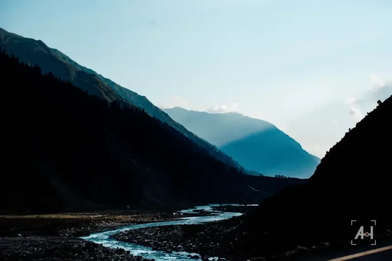 A river winding through a shadowed valley at dusk