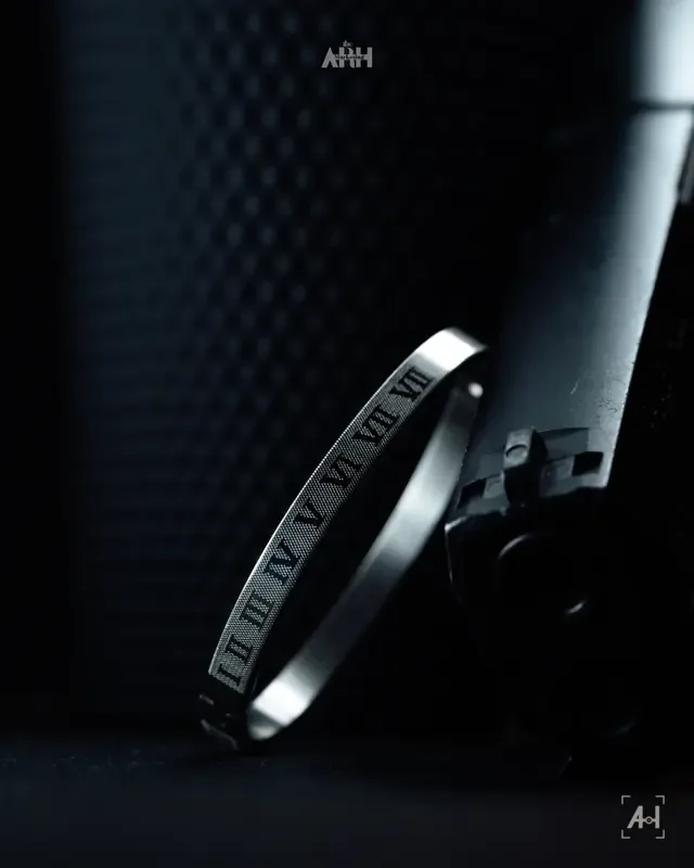 A steel Roman-numeral bangle leaning on black equipment in low light